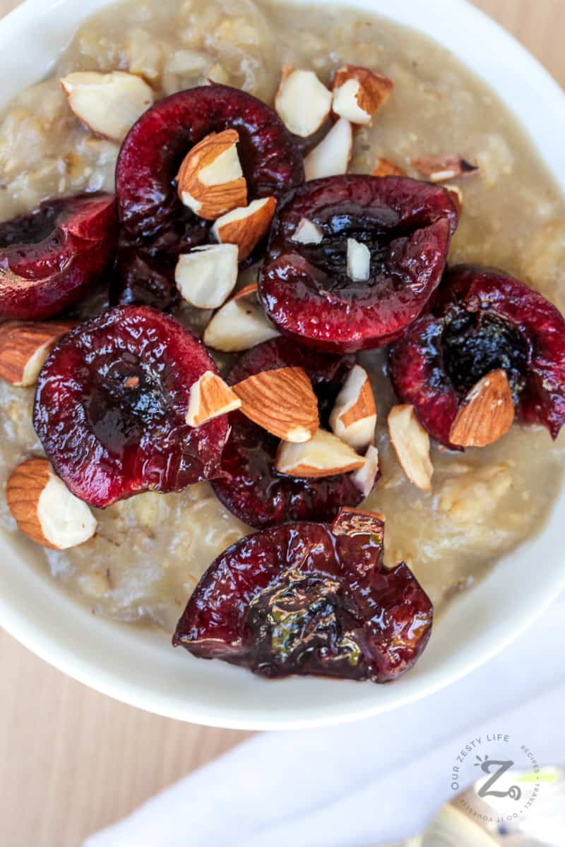 overhead view of 7 pitted cherries sliced in half on top of oatmeal and almond milk in a bowl