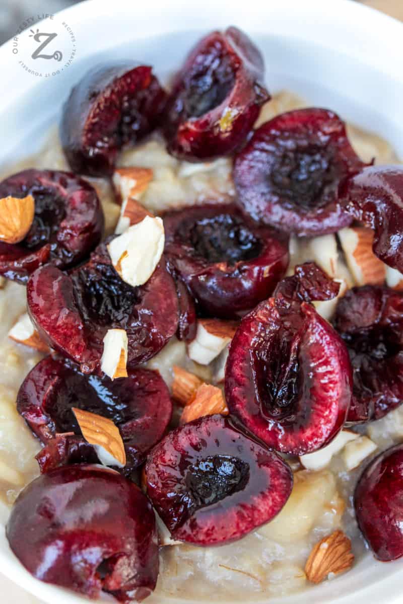 overhead view of 10-12 pitted cherries sliced in half on top of oatmeal and almond milk in a bowl