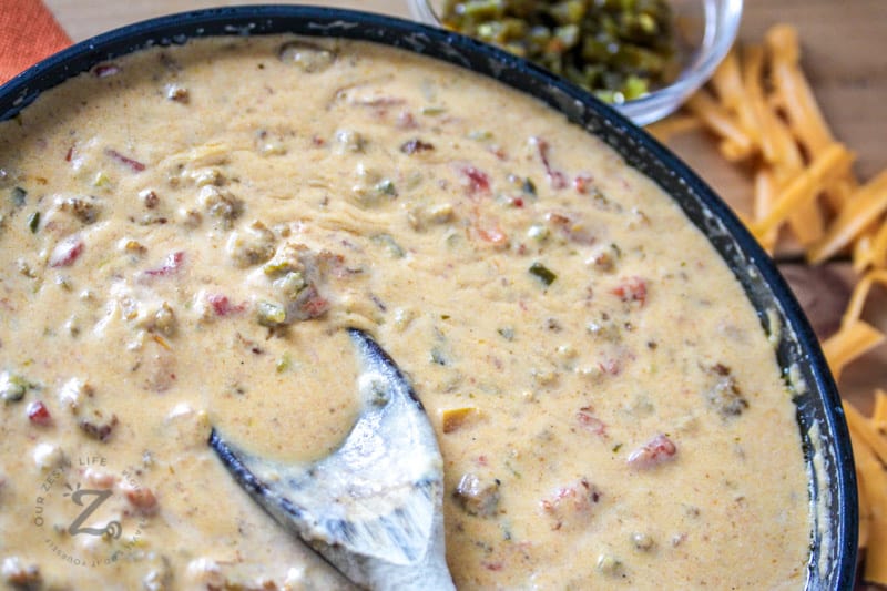 close up of queso cheese dip in a bowl with a spoon stirring the dip