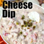 Queso cheese dip in a bowl with a cracker in the middle and finely chopped green chilies on top