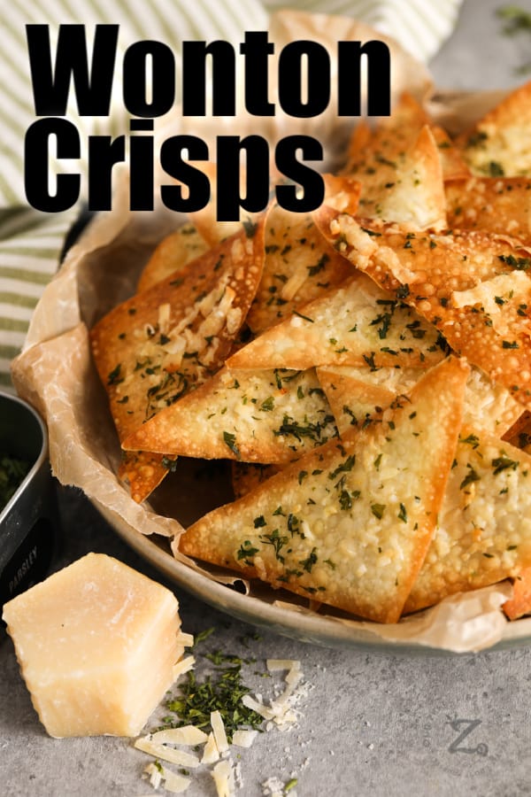 Baked wonton crisps in a bowl with parmesan and dried parsley in the foreground.
