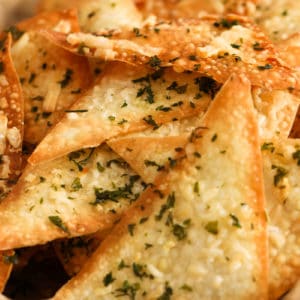 A close up of baked parmesan and parsley wonton crackers in a bowl.