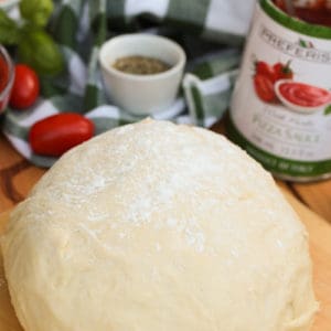 A ball of homemade pizza dough on a rolling board sprinkled with flour.