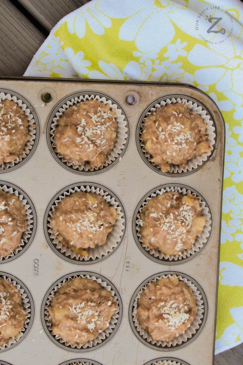 An overhead view of unbaked coconut banana muffins in a muffin tin with a towel in the background
