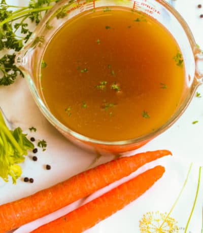 overhead view of finished turkey broth on a white counter with 2 carrots and parsley