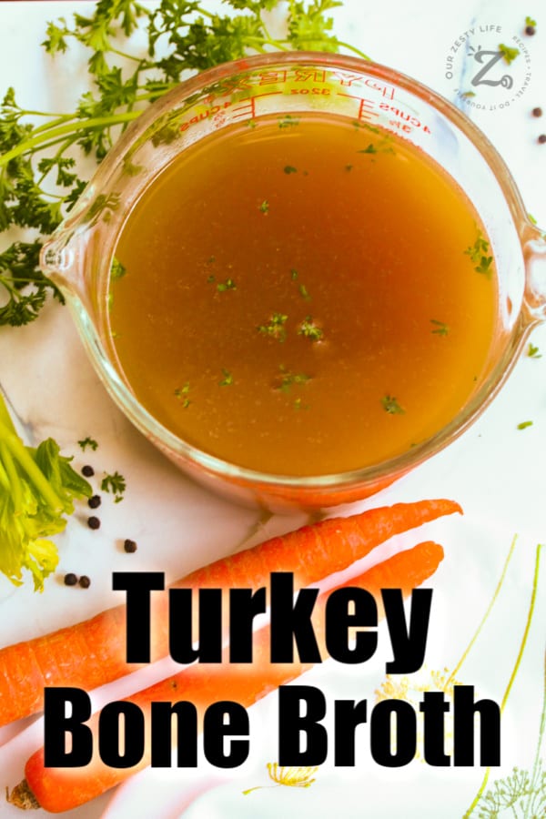 overhead view of turkey broth on a white counter and two carrots with parsley