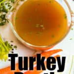 overhead view of turkey broth in a glass container on a counter with 2 carrots and parsley