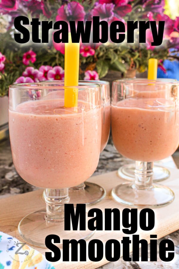 A close up of four strawberry mango smoothies on a tray with flowers in the background