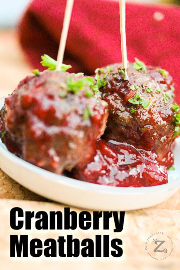 a close up of two cranberry meatballs with a toothpick in each on a small plate