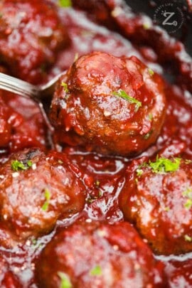 a close up of six cranberry meatballs in sauce one of which is in a spoon