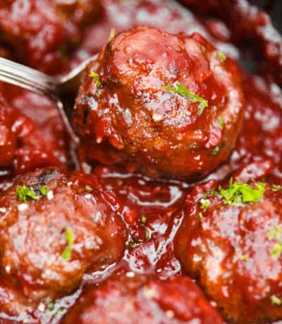 a close up of six cranberry meatballs in sauce one of which is in a spoon