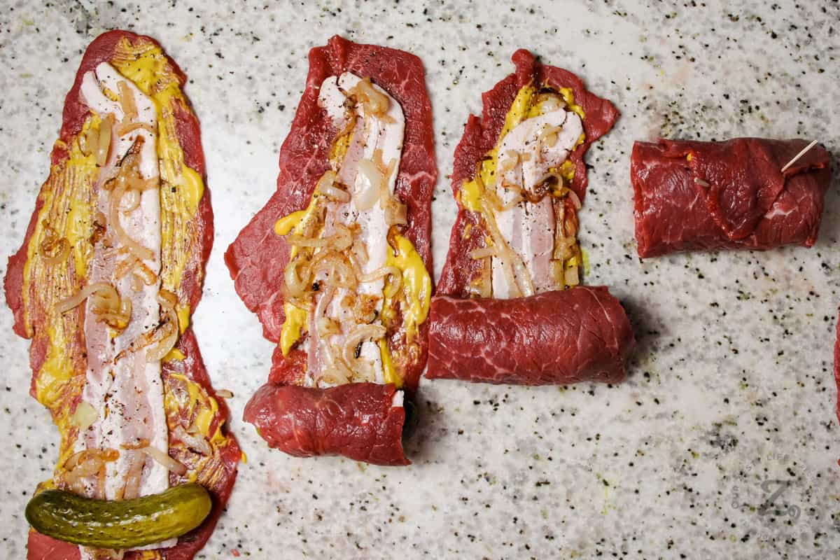 4 pieces of Beef Rouladen being rolled up on a marble board 