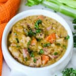 White bowl full of split pea and ham soup garnished with parsley