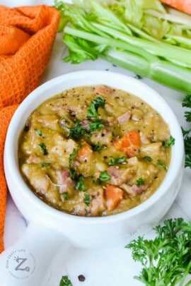 White bowl full of split pea and ham soup garnished with parsley