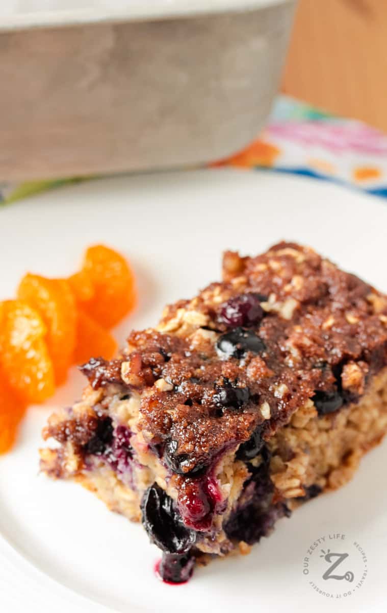 Square of blueberry banana baked oatmeal on a white plate with orange slices 