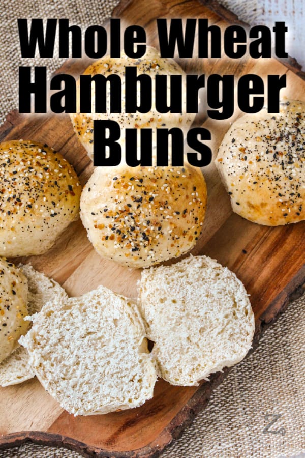 Hamburger buns on a wooden board with one sliced open with writing