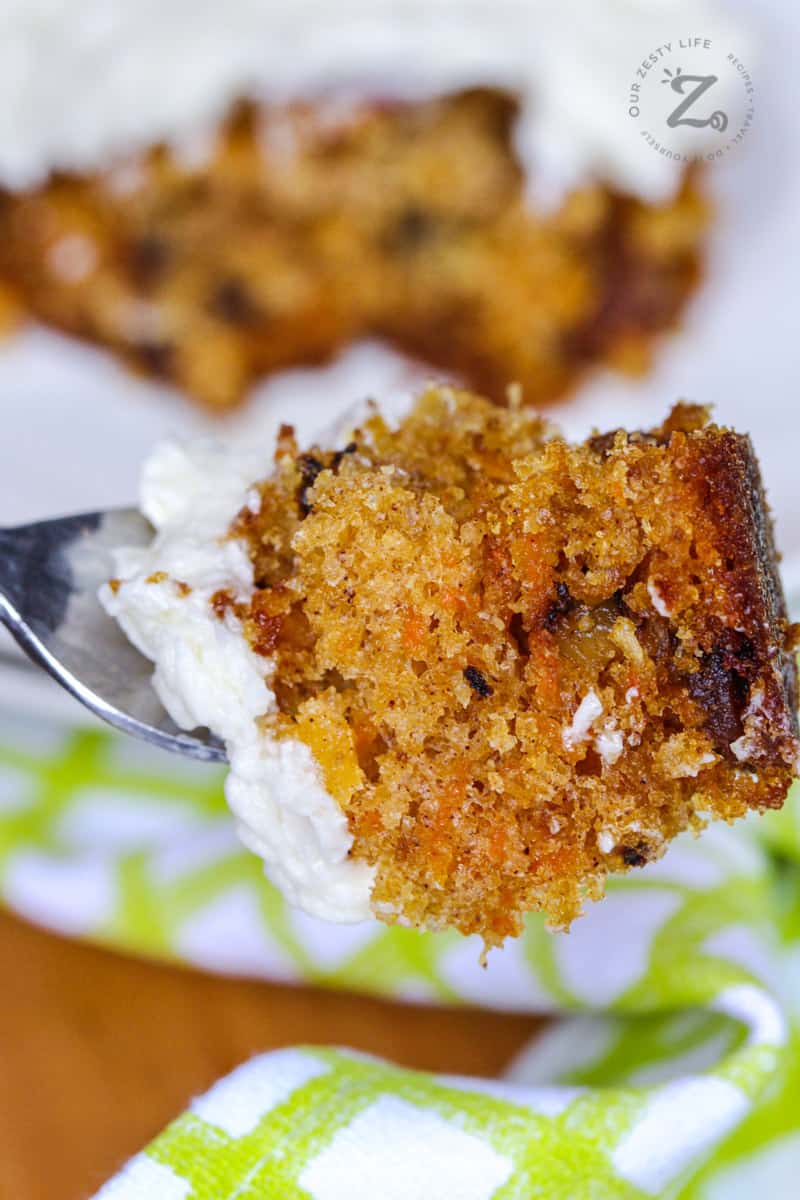Bite of homemade carrot cake with icing on a fork with cake in the background 