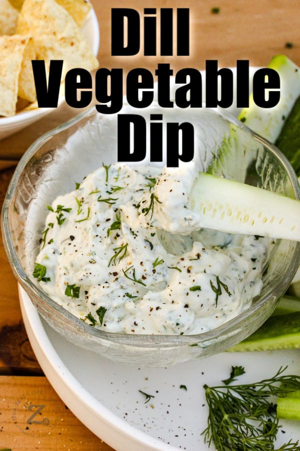 Veggie dip in a bowl with a piece of zuchini being dipped with sliced veggies in the background on a plate.