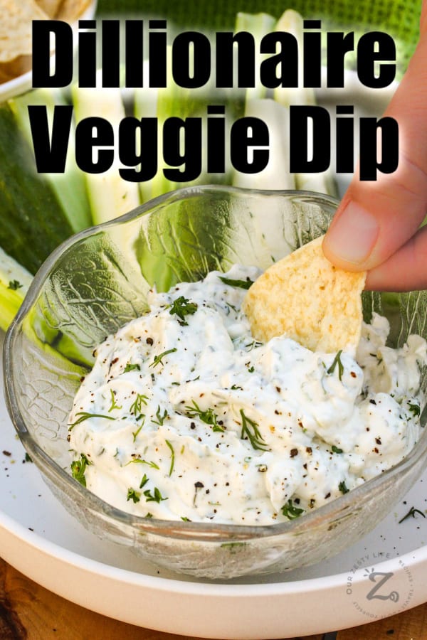 Veggie dip in a bowl with a chip being dipped with sliced veggies in the background on a plate.
