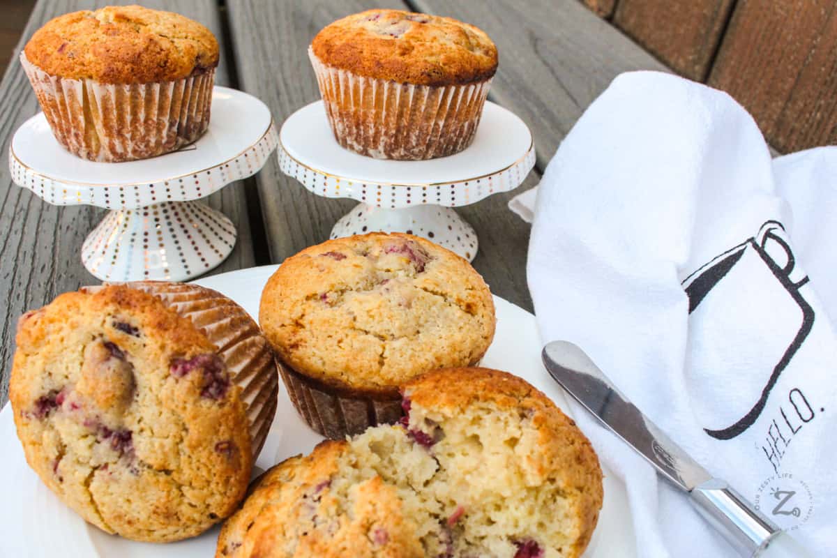 Raspberry Muffins on white serving plates with a butter knife and a white tea towel