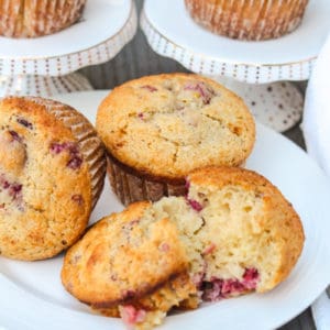 5 Raspberry Muffins on serving plates with one muffin cut in half