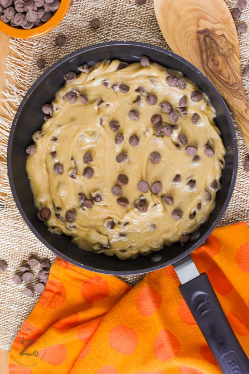 Raw pizookie in a pan with chocolate chips on the side