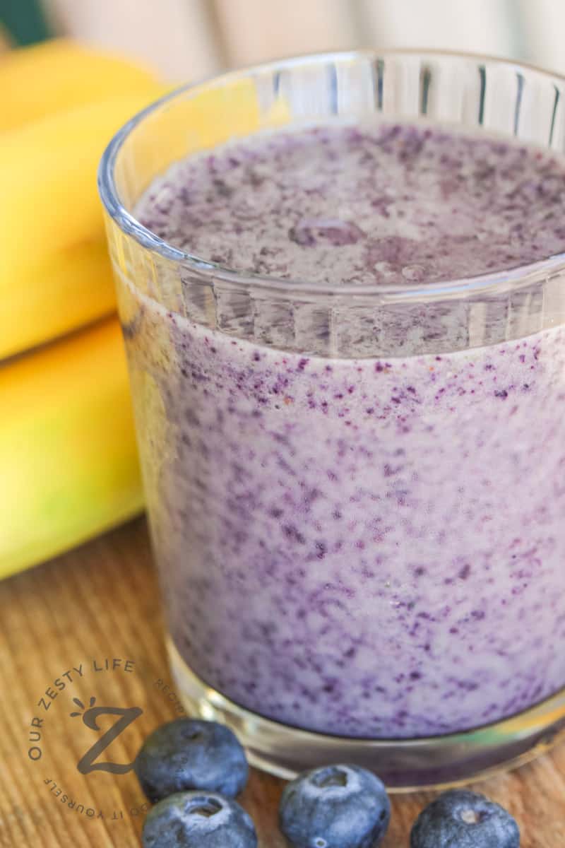 Blueberry Banana Smoothie in a glass on a wooden board with bananas and blueberries