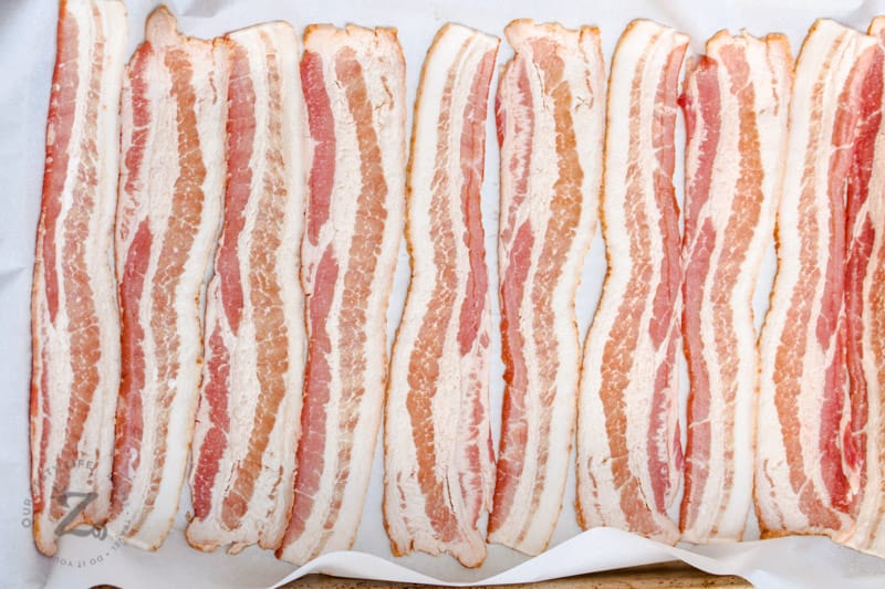 uncooked Bacon in the Oven on a baking sheet with parchment paper