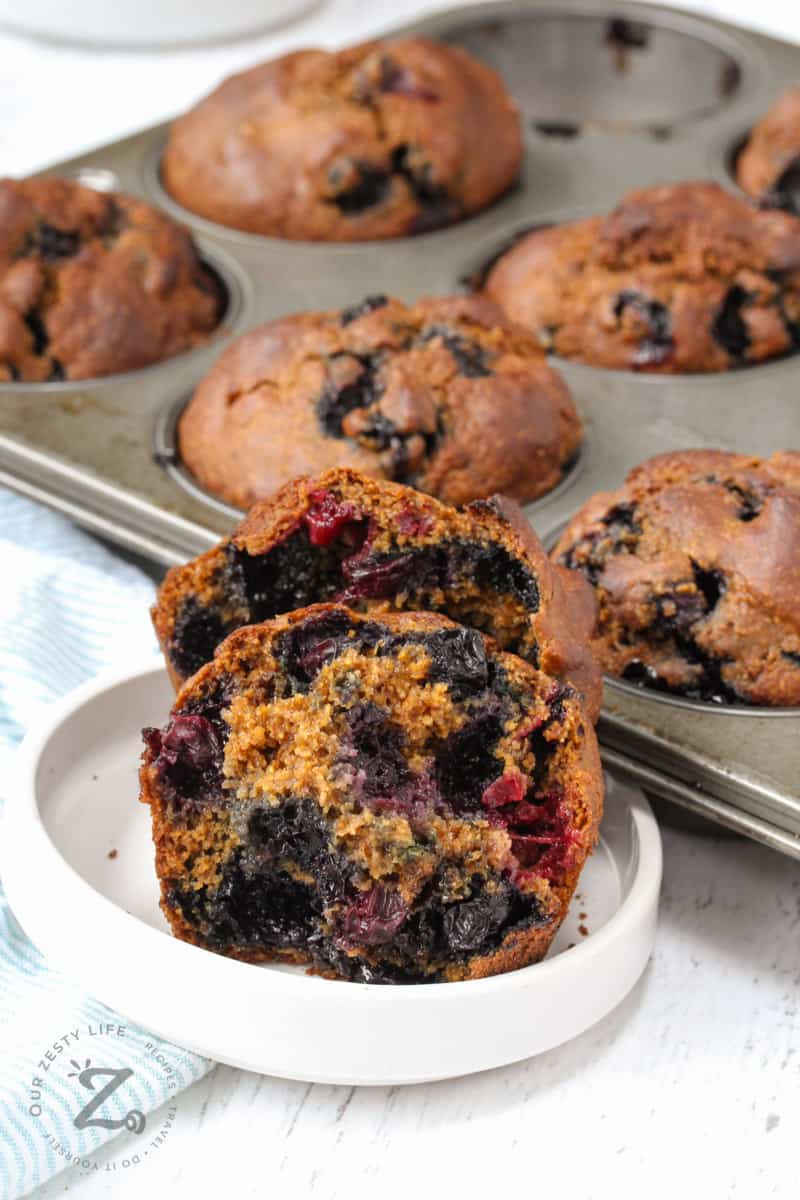 open Sourdough Blueberry Muffin in a dish with a baking sheet of muffins behind
