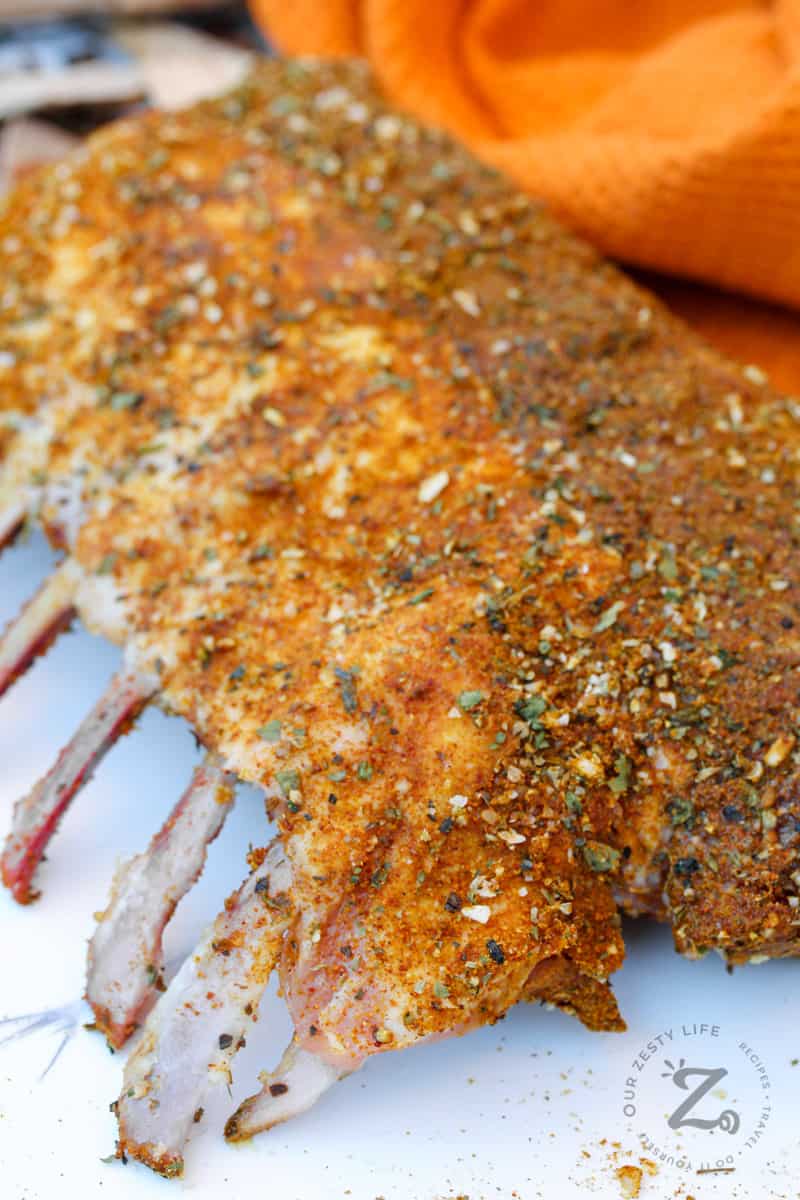 close up of Smoked Rack of Lamb on a white table with an orange cloth