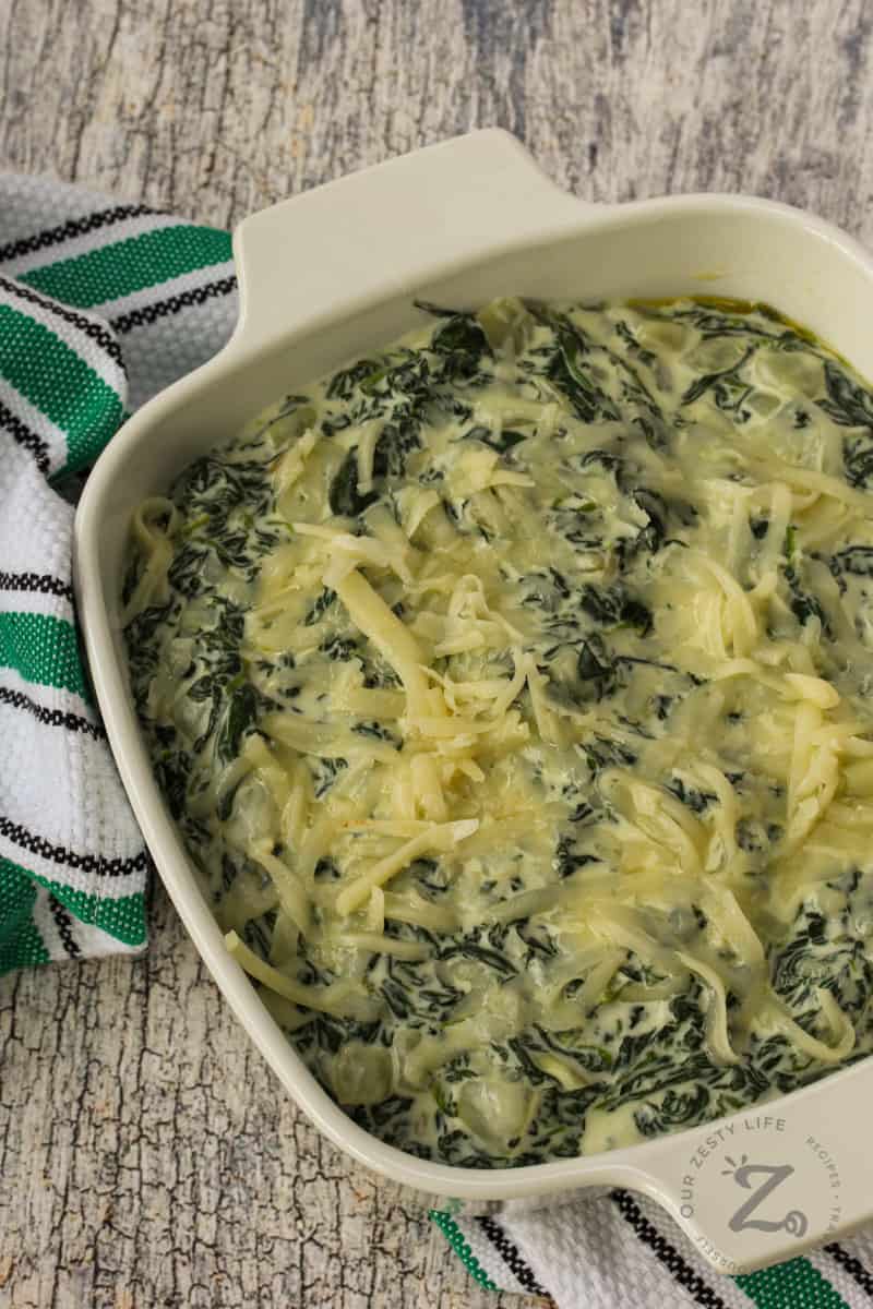 a casserole dish filled with spinach dip topped with cheese before being baked