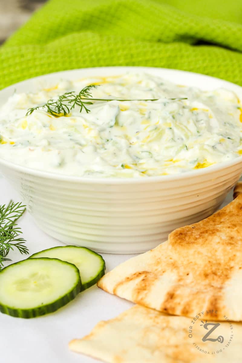 finished Tzatziki in a white bowl with cucumber and pita