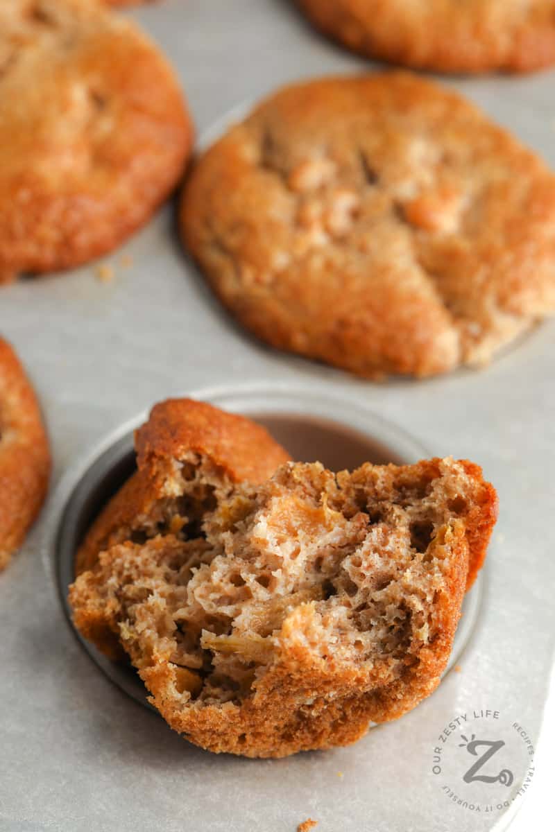 Peach Sourdough Muffins in a muffin tin with one muffin ripped in half