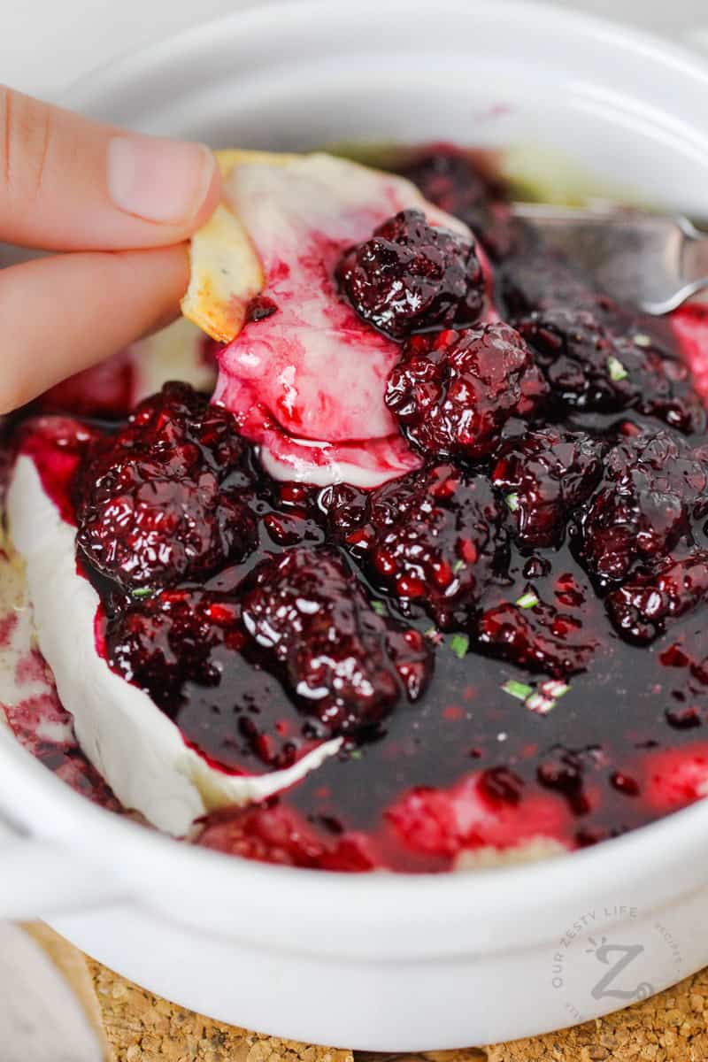 dipping a cracker in Baked Brie with Berries
