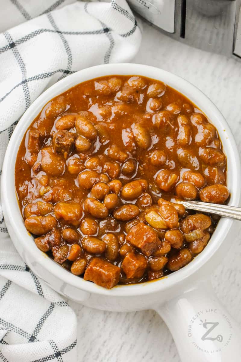 top view of Easy Slow Cooker Baked Beans in a white bowl with crockpot in the back