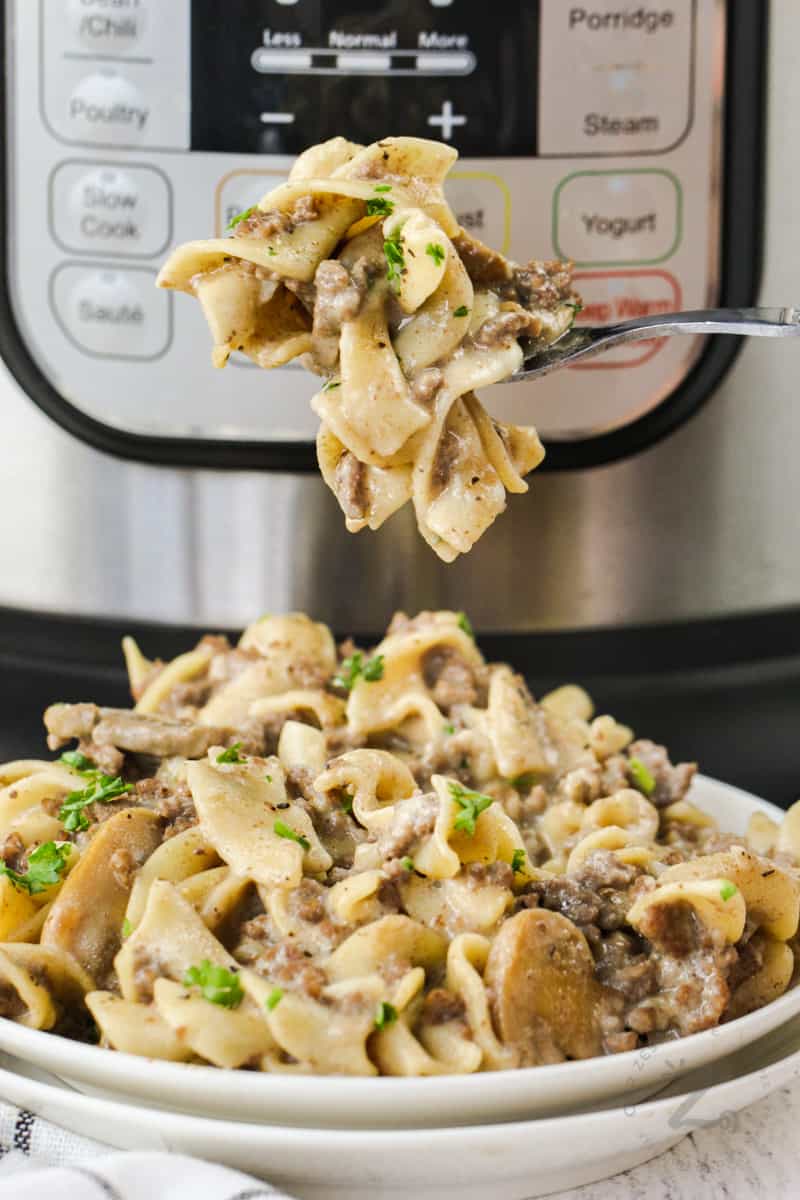 Instant Pot Ground Beef Stroganoff on a fork with a bowl full