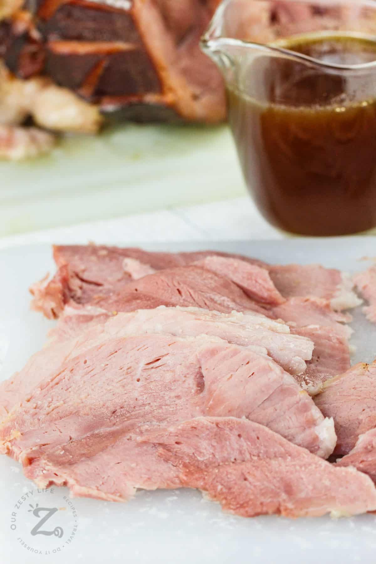 slices of Honey Glazed Baked Ham with a jar of glaze in the back