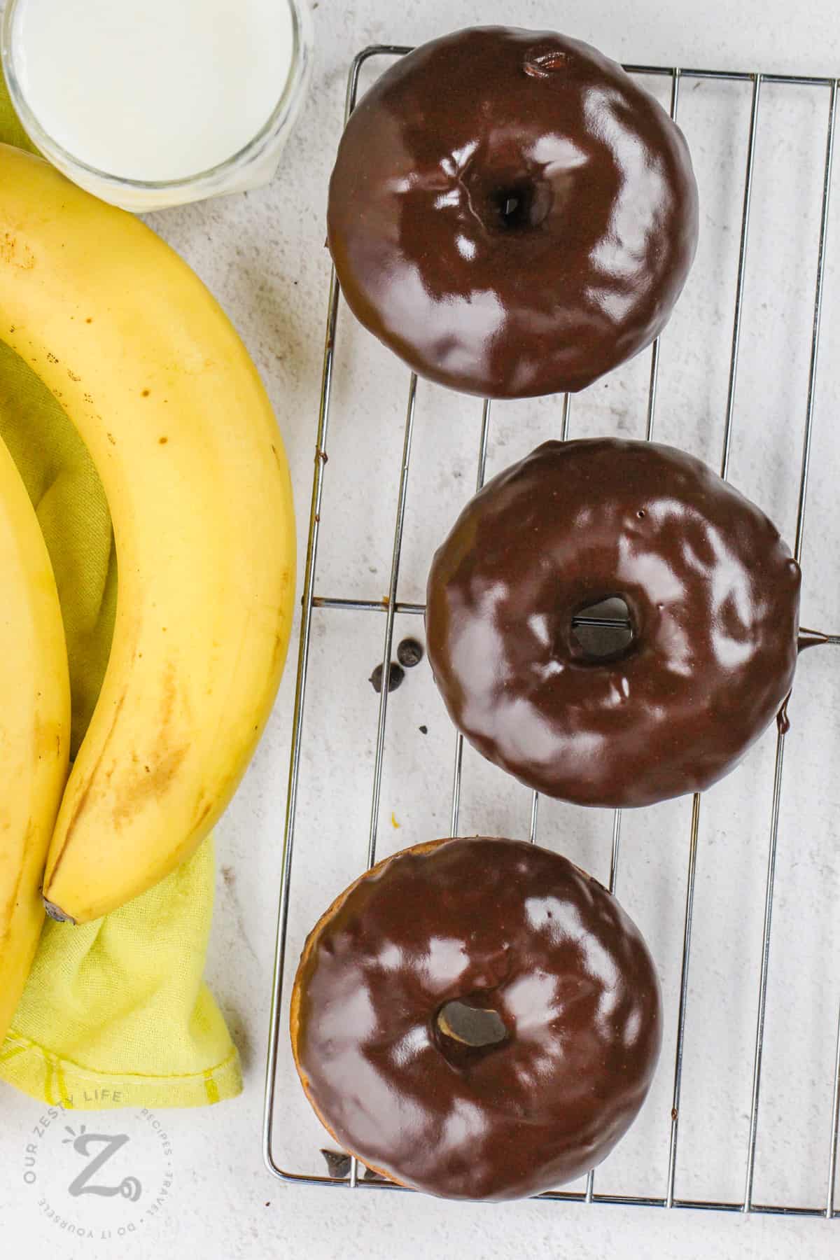 Banana Donuts with Chocolate Glaze cooling on a rack with bananas beside it
