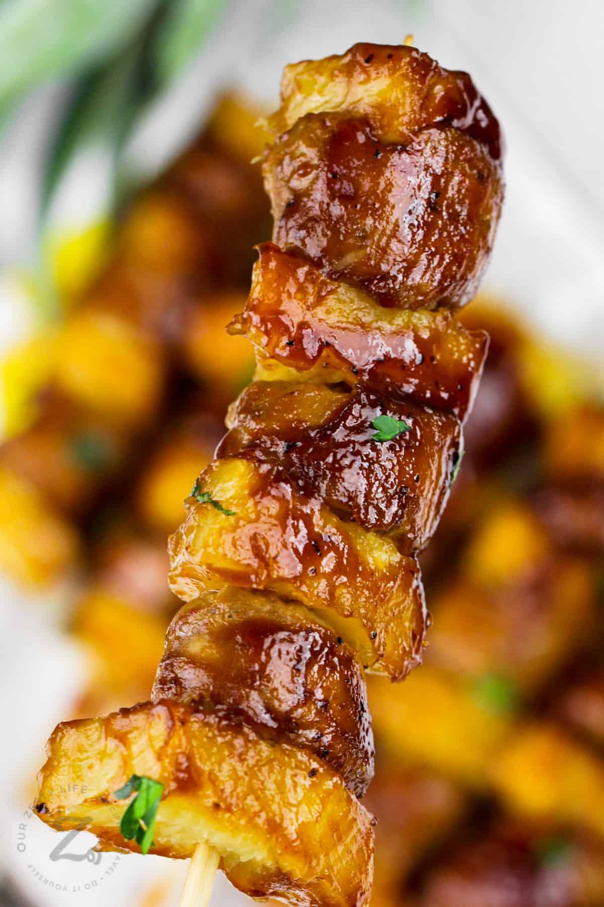 close up of Pineapple Sausage Skewers with plate full in the back