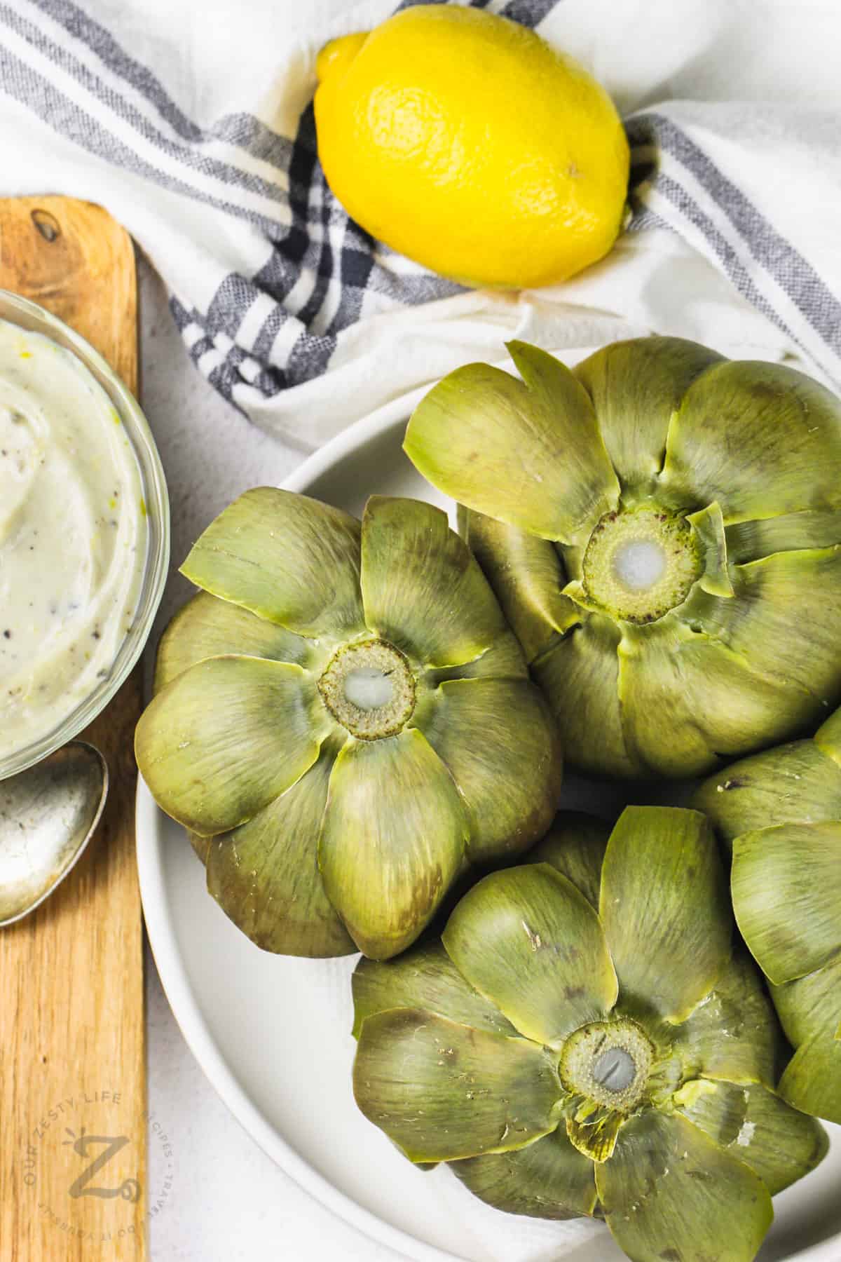 cooked Artichokes on a plate with dip and a lemon