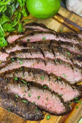 grilled flank steak sliced on a wooden board with a lime and cilantro on the side