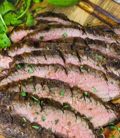 grilled flank steak sliced on a wooden board with a lime and cilantro on the side