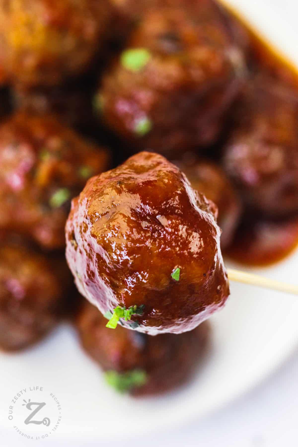 cooked Grape Jelly Meatballs on a toothpick and plate full in the back