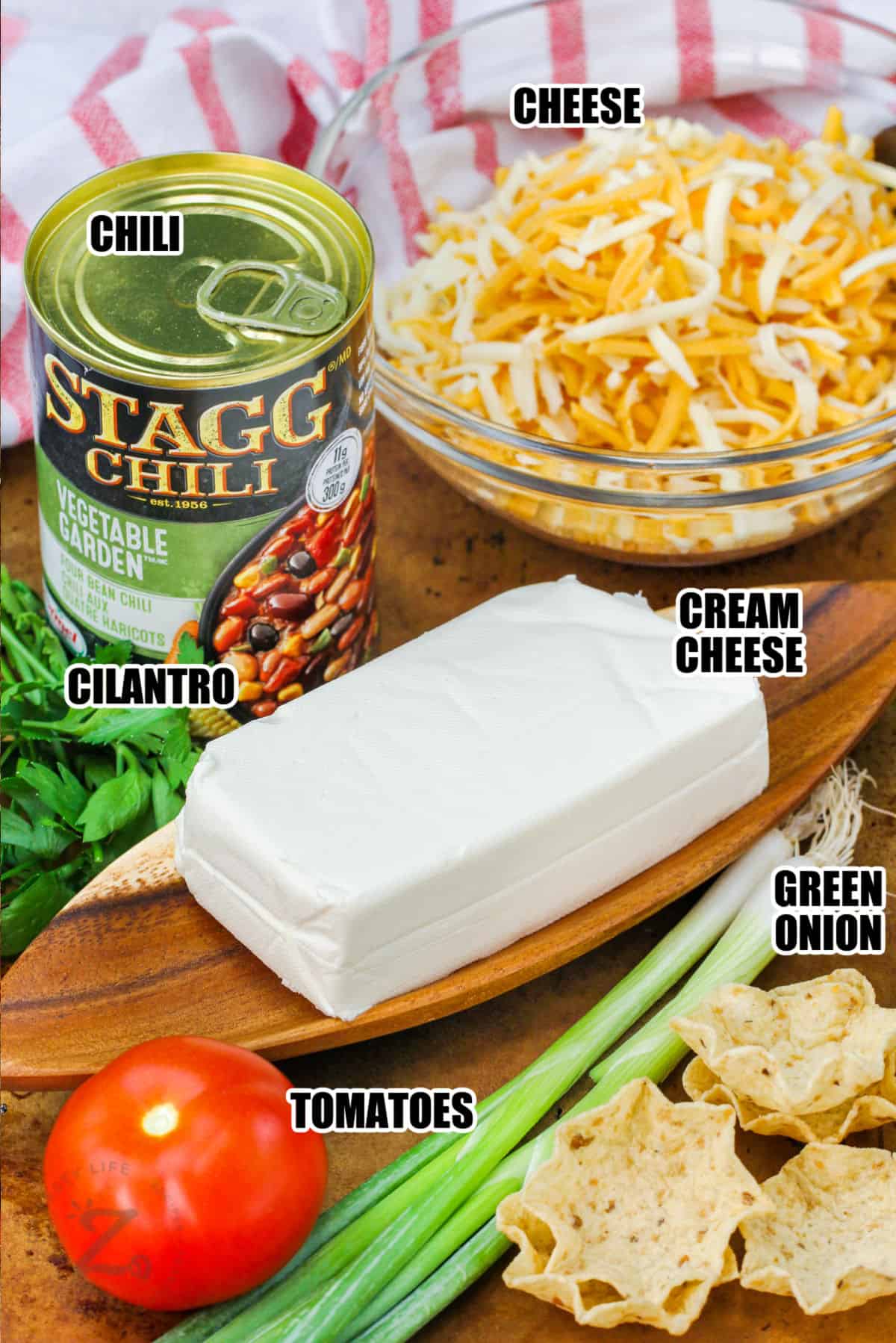 ingredients such as canned chili, shredded cheese, and cream cheese, cilantro, green onion and tomato, used to make Chili Cream Cheese Dip