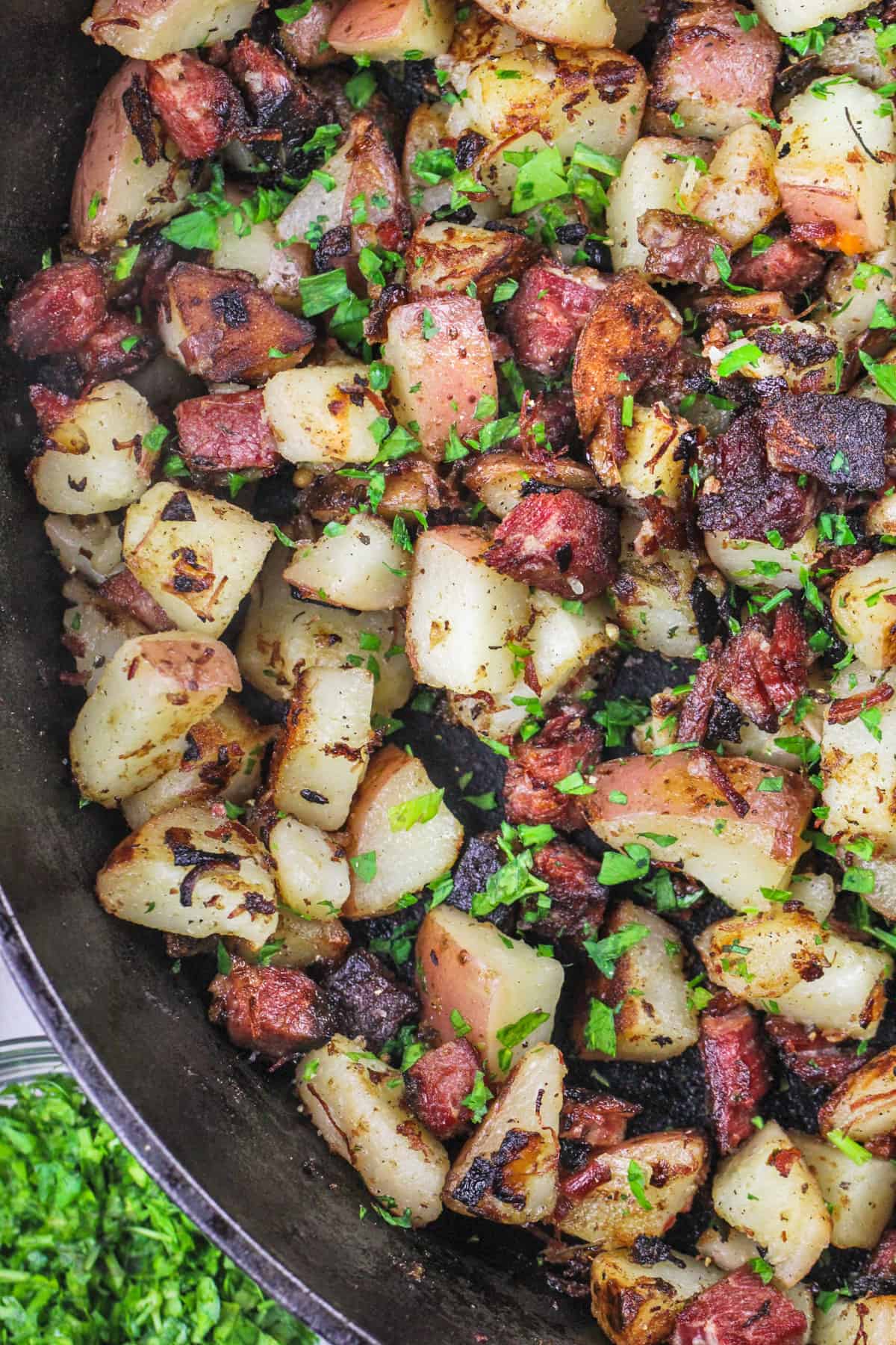 close up of corned beef hash in a cast iron frying pan, garnished with fresh parsley