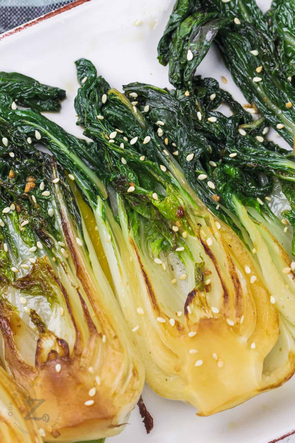 close up of garlic baby bok choy served on a rectangular dish, garnished with sesame seeds