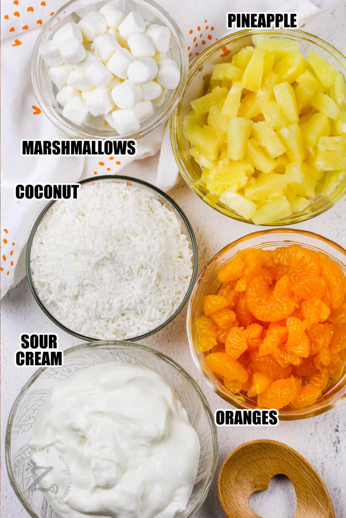marshmallows, pineapple, coconut, oranges, sour cream assembled to make ambrosia fruit salad