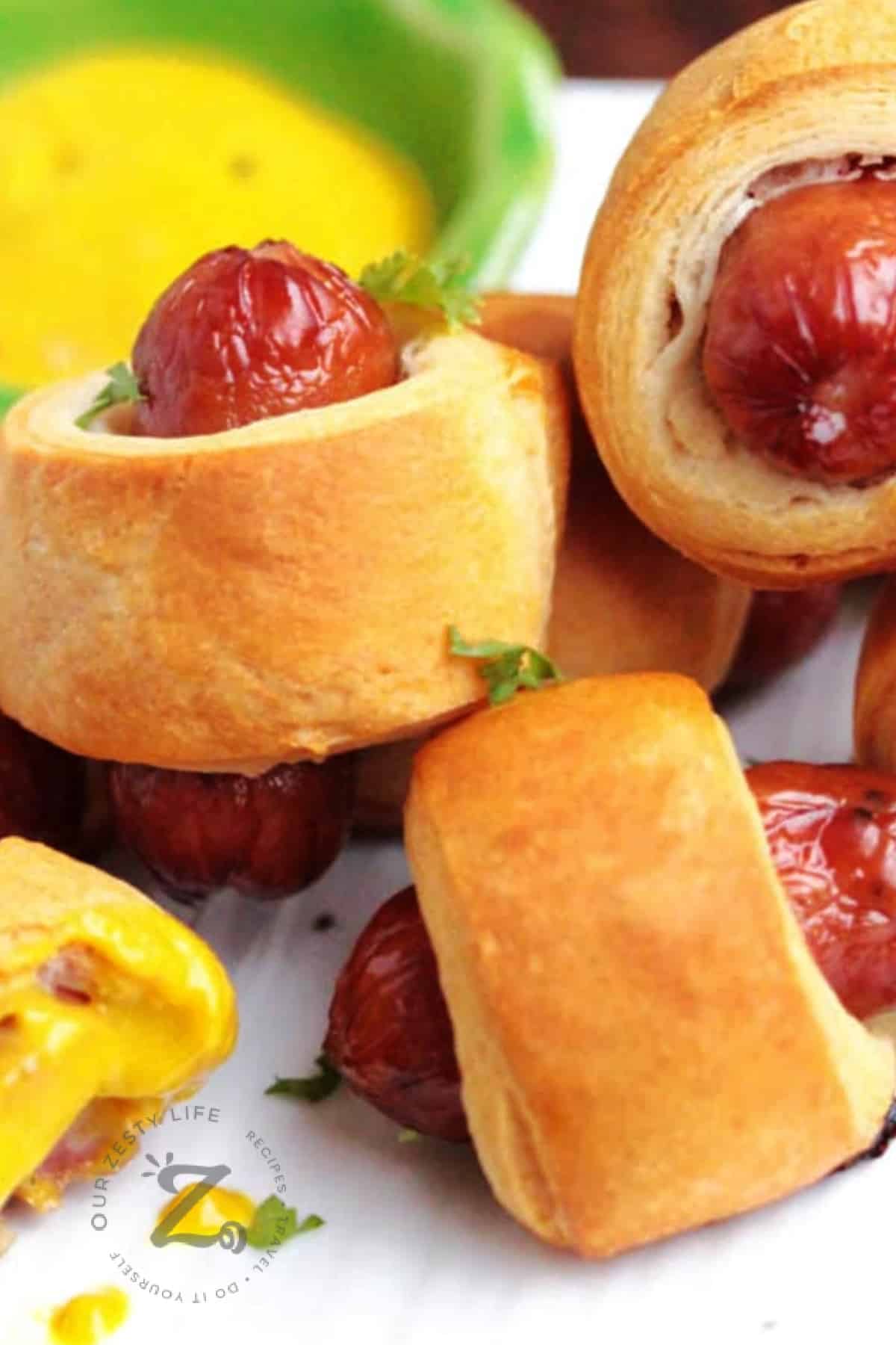 mini pigs in a blanket on a white plate with cheese dipping sauce in the background