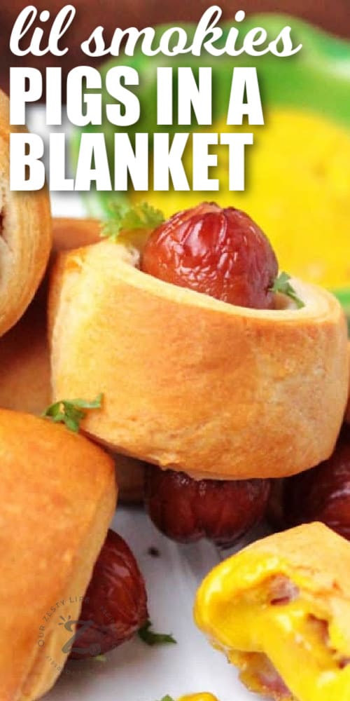 close up of mini pigs in a blanket on a white plate, garnished with parsley, with cheese dipping sauce in the background, with a title