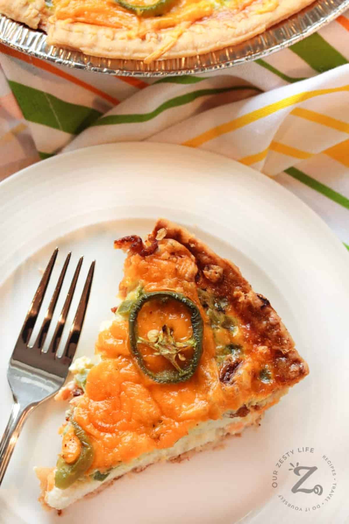zesty bacon and cheese quiche on a white plate with a fork and quiche in a pie plate on the side